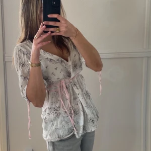 Somrig blus - Sååå fiin blus med rosa band och blomdetaljer, den skriker verkligen sommar!😍🥹 stl M men  passar S också när man knyter. Har vanligtvis XS och den passar ish bra, lite stor