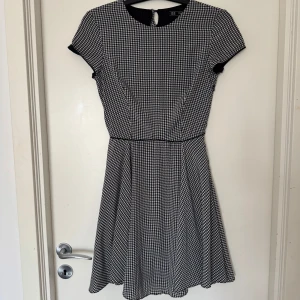 Svartvit rutig klänning från Trafaluc - Säljer en stilren svartvit rutig klänning från Trafaluc. Klänningen har korta ärmar och knappar längs ryggen. 