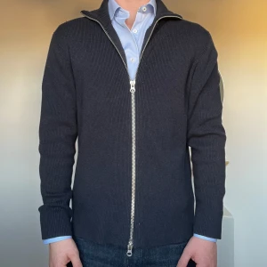 Mörkgrå ribbad kofta med dragkedja - Snygg mörkgrå kofta med dragkedja och ribbad struktur. Perfekt för lager-på-lager och har en stilren look. Passar bra över en skjorta för en mer dressad stil. Aldrig använd!! Helt ny! Köpt i Norge för 1999kr. 