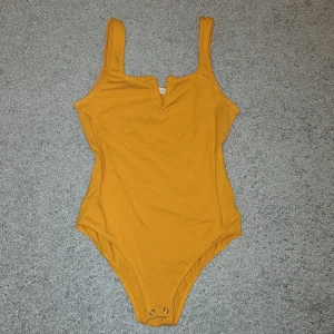 Bodysuit från Terranova - Säljer en snygg orange bodysuit från Terranova. Den har en liten v-ringning framtill. Perfekt för att styla med jeans eller kjol. Bodysuiten har knäppning för enkel på- och avtagning🙌