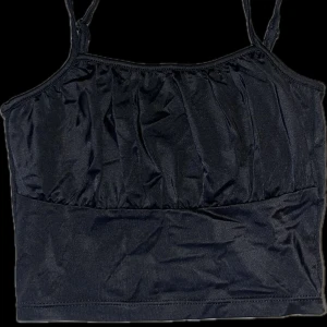 Svart linnetopp - Snygg svart croptop med smala axelband. Perfekt för varma dagar eller som ett lager under en jacka. Enkel och stilren design som passar till det mesta. 