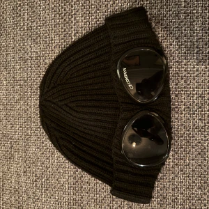 Cp Company mössa - Snygg svart mössa från C.P. Company med de klassiska glasögonen. Perfekt för kyligare dagar när man knte orkar fixa håret. Den är i size medium i juniorstorlek. Köpt på farfetch för 1200kr, säljer för endast 450kr 🤙🏼 Bara att höra av er om ni har några funderingar, pris kan diskuteras vid snabb och smidig affär 🙌🏼