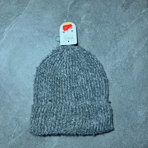 Grå stickad mössa  - Säljer en grå stickad mössa från. Mössan är tillverkad av 90% polyester och 10% ull, vilket gör den både varm och bekväm. Perfekt för kyliga dagar!