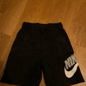 Svarta shorts från Nike - Säljer ett par svarta shorts från Nike med en stor vit logga på benet. Hör av dig vid funderingar!