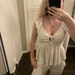 Vit blus med volangdetaljer - INTRESSEKOLL!! söt vit blus med volangdetaljer och knytning framtill. Blusen har en v-ringad design och är ärmlös.🩷🩷