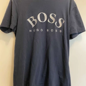 Mörkblå t-shirt från Hugo Boss - Snygg mörkblå t-shirt från Hugo Boss med stort tryck på bröstet. Perfekt för en stilren och avslappnad look. Passar bra till jeans eller shorts.
