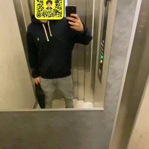 Mörkblå hoodie från Ralph Lauren - Säljer en snygg mörkblå hoodie från Ralph Lauren med det klassiska gula logotypen på bröstet. Tröjan har en justerbar huva med vita snören och långa ärmar. Perfekt för en avslappnad stil.