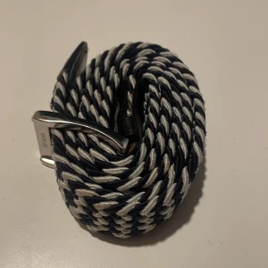  flätat bälte - Snyggt flätat bälte med ett randigt mönster i svart och vitt. Bältet har ett stilrent silverfärgat spänne som ger en modern touch. Perfekt för att ge din outfit det lilla extra.