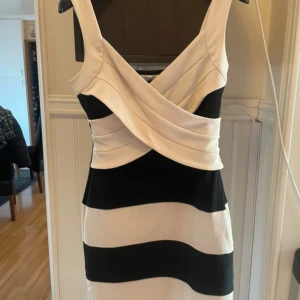 Svartvit klänning från Oneness - Snygg svartvit klänning från Oneness med breda horisontella ränder och omlott-design vid bysten. Perfekt för en stilren look.