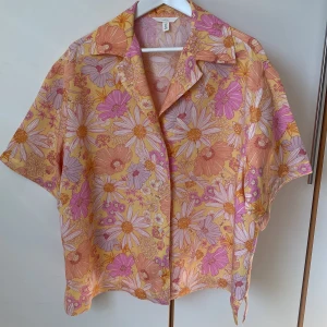 Sommarens gladaste linneskjorta - Glad blommig skjorta från H&M i linneblandning. Skjortan är en härlig mix av rosa, orange och gult med stora blommor. Vid modell och vida ärmar. Längd 69 cm, axelbredd 51, vidd omkrets 130. Använd en gång, tvättad en gång. 