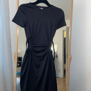 Svart klänning med knytning - Snygg svart klänning med knytning i midjan som ger en smickrande passform. Kortärmad design med en stilren look. Perfekt för olika tillfällen.