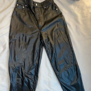 Svarta skinnbyxor från H&M - Snygga svarta skinnbyxor från H&M med hög midja och raka ben. Byxorna har klassisk femficksdesign och stängs med dragkedja och knapp. Perfekta för en trendig look!