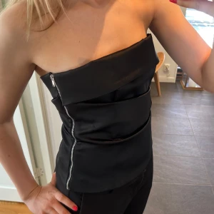 Svart topp med dragkedja - Säljer en snygg svart axelbandslös topp med dragkedja på sidan från Zara. Använd endast en gång💕