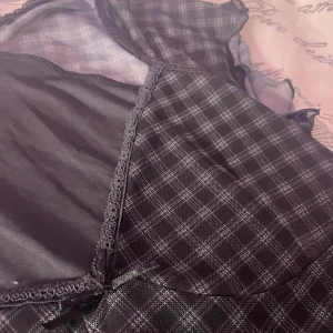 Svart och grå rutig topp från HM - Säljer en snygg svart och grå rutig topp från HM. Toppen har korta ärmar i mesh och en v-ringad design med spetsdetaljer. Perfekt för en stilren look.