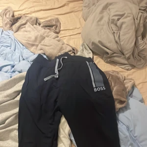 Svarta mjukisbyxor från BOSS M - Snygga svarta mjukisbyxor från BOSS med grå dragsko i midjan och coola grå ränder samt BOSS-logga på ena benet. Sköna och stilrena byxor i mjukt material, perfekta för chill eller träning.