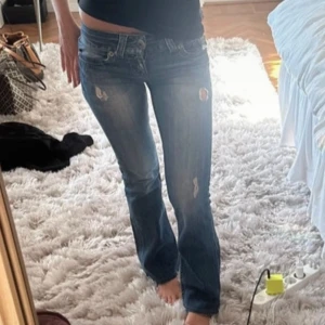 Blå bootcut jeans från Guess, stl 25 - Säljer ett par snygga blå bootcut jeans från Guess Premium. Jeansen har slitna detaljer, klassisk femficksdesign och ikonisk Guess-logga på bakfickan. Knappen åker av ibland men det är bara att stoppa in den i hålet igen. Midjemått: 35cm och inerbenslängd: 75cm. 