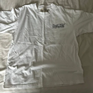 Vit Yacht Club t-shirt med tryck - Vit t-shirt från Yacht Club Notre Succès med svart tryck fram och stor Dolce Vita Portofino-grafik på ryggen. Klassisk passform, rund hals och korta ärmar. Perfekt för dig som gillar en clean look med coola detaljer. Materialet känns mjukt och skönt. OBS Den är L Men sitter lite mer som M