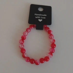 Rött pärlarmband med glittriga detaljer - Handgjort armband med röda och glittriga pärlor på elastisk tråd. Pärlorna är runda och varvas mellan klara röda och spräckligt glittriga pärlor för en snygg effekt. Perfekt accessoar för att lyfta din outfit.