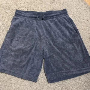 Mörkblå frottéshorts från lager 157 - Mysiga mörkblå shorts från lager 157 i mjuk frotté. De har elastisk midja med snörning och två sidofickor. Perfekta för chill dagar eller efter träning. Klassisk och enkel design som är lätt att matcha med t-shirt eller hoodie. Storlek 160. 