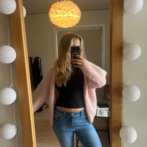 Ljusrosa cardigan jacka från Lindex - Supermjuk och fluffig ljusrosa cardigan jacka från Lindex. Den har en loose passform, är långärmad och stickad i ett gosigt material. Perfekt att slänga på sig över en topp för en chill och söt look. Bra skick!!
