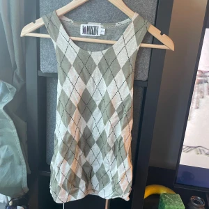 Rutig ärmlös topp från No Parking - Snygg ärmlös topp från No Parking med rutigt mönster i beige och olivgrönt. Toppen har rund halsringning och är stickad i mjukt material, perfekt för en trendig och avslappnad look. Passar dig som gillar preppy vibes och vill sticka ut lite extra.