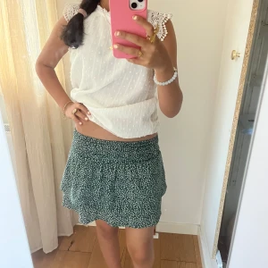 Grön blommig kortkjol med volang - Supersöt grön kortkjol med små vita blommor och volangkant. kjolen har inbyggda shorts vilket är skit smart så om kjolen blåser upp så syns ingenting man inte vill. 