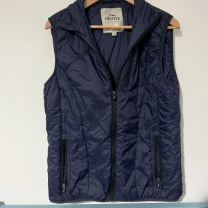 Mörkblå dunväst från Protech - Snygg mörkblå dunväst från Protech med dragkedja framtill och två praktiska fickor med dragkedja. Västen har en sportig look och är lätt vadderad, perfekt för lager-på-lager. Passar dig som gillar en aktiv stil. Öppen för bundles och frågor!  Man, kille, grisch, Stockholm, plagg, billigt, small, s, stil, stiligt, style, jacka, tröja, skjorta, kvalitet, märke, märkeskläder