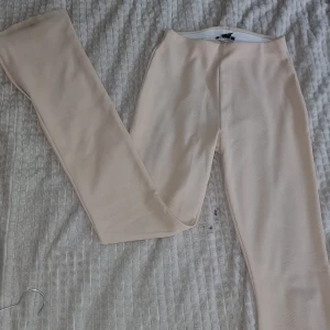 Beige utsvängda byxor med slits (flared) - Utsvängda beige byxor i ribbat material med hög midja och raka ben. Byxorna har en diskret slits nertill på benen som ger en trendig touch. Perfekta att styla med sneakers eller boots för en chill look.