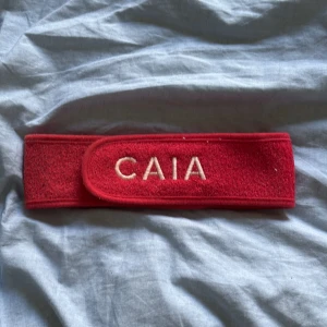 Rött smink band från CAIA med kardborre - Snyggt rött diadem från CAIA med broderad logga framtill. Tillverkat i mjuk frotté och har praktisk kardborrestängning för enkel användning. Perfekt när du vill hålla håret borta vid sminkning eller hudvård. Säljer samma fast i rosa också 