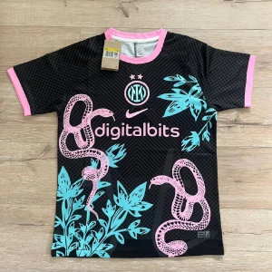 Inter Milan x Nike svart fotbollströja  - Inter Milan fotbollströja från Nike i svart med rosa och turkosa detaljer. Tröjan har korta ärmar, rosa ormmotiv och turkosa blad på framsidan, samt rosa muddar och krage. Digitalbits-logga och klubbmärke på bröstet. 