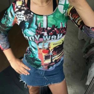 Färgglad mesh topp med New York-tryck - Säljer en långärmad mesh topp med färgstarkt New York-motiv och collage-tryck i grönt, blått, rött och svart. Toppens material är tunn och stretchig mesh, perfekt för dig som gillar statement-plagg och coola prints.