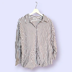 Randigt set i storlek L från Kappahl - Brun- och vitrandigt set från Kappahl bestående av en skjorta och ett par shorts. Skjortan har långa ärmar och knäpps framtill. Shortsen har resår, dragkedja och en knapp i midjan. Aldrig använt.