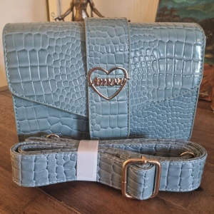 Amour Axelremsväska  - Snygg vintage turkos axelväska från Amour med croco-mönstrad yta i syntetmaterial. Justerbar axelrem och stängs med magnetlås. Mått: 21 cm x 6 cm x 14 cm. 