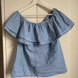 Ljusblå offshoulder topp Gina Tricot - Supersöt ljusblå offshoulder topp från Gina Tricot med bred volang runt axlarna. Toppen är ärmlös och har en luftig passform. Tröjan är i storlek 34