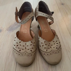 Beige klackskor - Säljer ett par beige klackskor från Simona fashion i skinn med utskurna detaljer och en rem runt ankeln. Skorna har låg klack och en rund tå. Osäker på storleken men de passar mig bra som brukar ha storlek 37💕