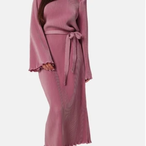 Rosa ribbad långklänning med bälte - Superfin rosa långklänning med ribbad struktur och matchande bälte i midjan. Klänningen har långa ärmar med lätt utsvängda ärmslut och vågig kant nertill. Perfekt för dig som gillar en stilren men ändå trendig look. Endast provad.
