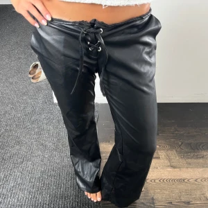 Svarta skinnbyxor med snörning - Snygga svarta lågmidjade skinnbyxor med cool snörning framtill i midjan