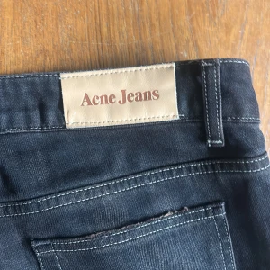 Svarta jeans från Acne Jeans - Säljer ett par svarta jeans från Acne Jeans med klassisk femficksdesign och snygga sömdetaljer vid knäna, då dem har blivit för små för mig. Jeansen har raka ben och tydliga kontrastsömmar. Perfekta för dig som gillar stilrena och tidlösa jeans med en modern touch.