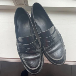 Svarta loafers i skinn med crocomönster - Klassiska svarta loafers i skinn med crocomönstrad yta och rund tå. Snygg och chunky sula som ger en cool vibe till outfiten. Perfekta att styla med både jeans och kostymbyxor för en trendig look.