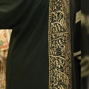 Svart klänning med broderade gulddetaljer - Säljer en svart långklänning med breda, broderade gulddetaljer längs ärmslut och framtill. Klänningen har en rak passform och är öppen framtill, perfekt för dig som gillar unika och traditionella inslag i din stil.