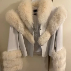 Vit jacka/ skin med päls  - Säljer en vit jacka med lyxiga, fluffiga päls  vid krage, ärmslut och längs framsidan. Jackan är croppad och har en elegant, figurnära passform. Perfekt för dig som vill sticka ut med en statementjacka.
