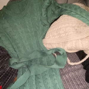 Grön stickad klänning med bälte - Mysig grön stickad klänning med kabelstickat mönster och matchande bälte i midjan. Rund halsringning och lång ärm, perfekt för kyligare dagar. Snygg och enkel att styla med boots eller sneakers.