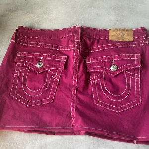 True religion kjol - Snygg rosa kjol från True Religion med kontrasterande vita sömmar och dekorativa ficklock med knappar. har en klassisk femficksdesign och en unik stil som sticker ut.