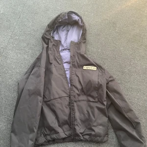 Svart jacka från Capeesh - Säljer en svart jacka från Capeesh som går att vända ut och in med huva och dragkedja. Jackan har två stora fickor framtill. Perfekt för kalla och lite varmare dagar och enkel att matcha med olika outfits. Modellen är giacca 8