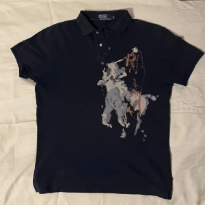 Mörkblå pikétröja med tryck från Ralph Lauren - Säljer en mörkblå pikétröja från Ralph Lauren med stort tryck av en polospelare på framsidan. Väldigt sällsynt.