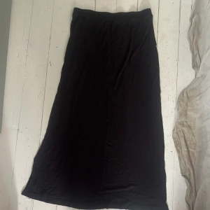 Svart långkjol i mjukt material - En svart långkjol med enkel och stilren design. Kjolen har rak passform och resår i midjan för extra komfort. Perfekt att matcha med en crop top eller stickad tröja.Väldigt luftig 