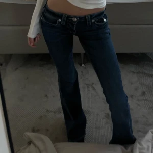 True Religion Joey Low Rise Flare Jeans - Säljer ett par mörkblå True Religion Joey jeans med låg midja och utsvängda ben. Klassiska kontrastsömmar och detaljerade bakfickor med lock och knapp. Nyskick, använda 2 gånger! 