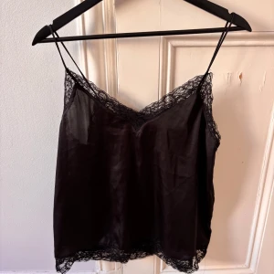 Svart linnetopp med spetsdetaljer - Säljer en svart linnetopp med tunna axelband och fina spetsdetaljer! 