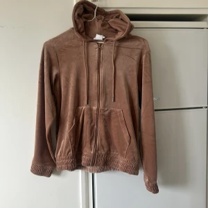 Brun hoodiejacka med dragkedja - Mjuk och skön brun hoodiejacka med dragkedja framtill och huva med snörning. Jackan har långa ärmar, två fickor och resår vid ärmslut och nederkant. Perfekt för en avslappnad stil.