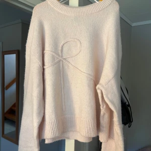 Ljusrosa stickad tröja med rosettdetalj från Divided - Superfin ljusrosa stickad tröja från Divided med en söt rosettdetalj framtill. Tröjan har lång ärm, rund halsringning och breda ribbade muddar vid ärmslut och nederkant. Perfekt för mysiga dagar! Den är knappt använd och är i ett väldigt bra skick. Kontakta för frågor💗